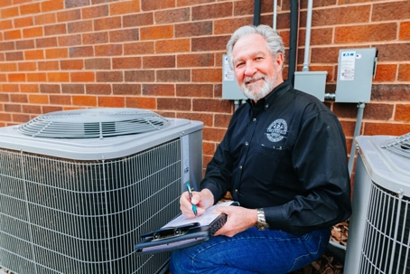 A man sitting next to an air conditioning unit